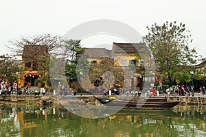 View on the embankment of Thu Bon River with yellow buildings and traditional wooden boats.