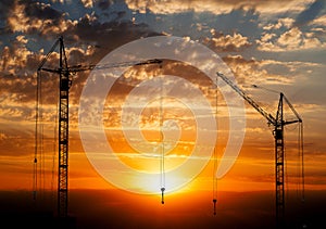 Hoisting cranes working on beautiful cloudy sky with orange sunset photo