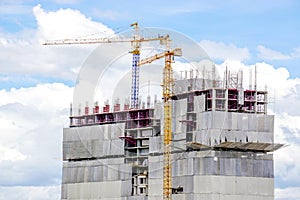 Hoisting cranes working building construction on bright blue sky and big cloud background