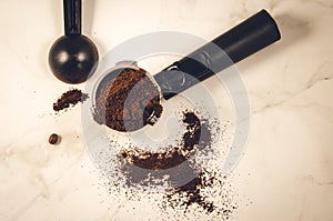 Holder filled with ground coffee a black spoon/holder filled with ground coffee a black spoon on a marble background. Top view