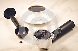 holder filled with ground coffee, spoon and cup/ holder filled with ground coffee, spoon and cup on a marble background