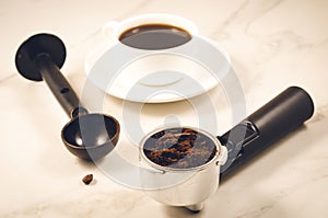 Holder filled with ground coffee, spoon and cup/holder filled with ground coffee, spoon and cup on a marble background