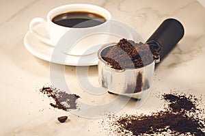 Holder filled with ground coffee and a white cup/holder filled with ground coffee and a white cup on a marble background.