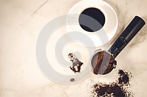 Holder filled with ground coffee and a white cup/holder filled with ground coffee and a white cup on a marble background. Top view