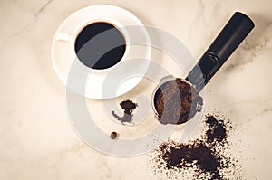 Holder filled with ground coffee and a white cup/holder filled with ground coffee and a white cup on a marble background. Top view