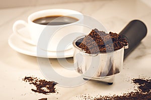 Holder filled with ground coffee and a white cup/holder filled with ground coffee and a white cup. Selective focus