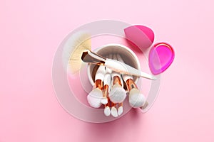 Holder with professional makeup brushes and sponges on pink background