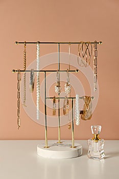 Holder with set of luxurious jewelry and perfume on white table near pale pink wall