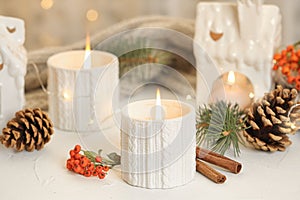 Holders with burning candles and decoration on table against blurred Christmas lights