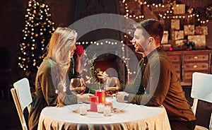 Holding beautiful red rose. Young lovely couple have romantic dinner indoors together