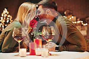 Holding beautiful red rose. Young lovely couple have romantic dinner indoors together