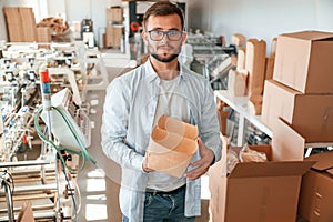 Holding beautiful wooden packages. Print house worker in white clothes is indoors