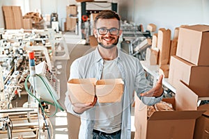 Holding beautiful wooden packages. Print house worker in white clothes is indoors