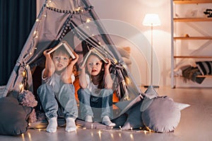 Holding books on head. Playful mood. Two little girls is in the tent in domestic room together