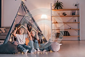 Holding books on head. Playful mood. Two little girls is in the tent in domestic room together