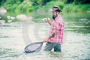 Holding brown trout. Man with fishing rods on river berth. Men fishing in river during summer day. Fly fisherman using