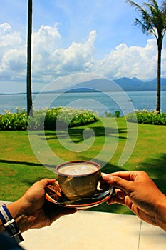 Holding cappuccino coffee in the morning on the beach when the blue sky is bright.