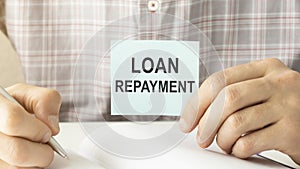 Holding a card with LOAN REPAYMENT message, business concept image with soft focus background