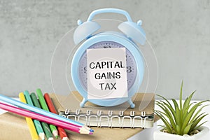 Holding a card with text CAPITAL GAINS TAX on alarm clock , business concept image with soft focus background