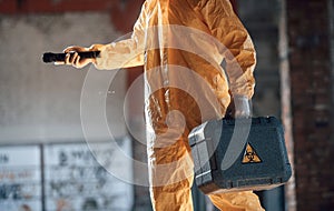 Holding case and flashlight. Man dressed in chemical protection suit in the ruins of the post apocalyptic building