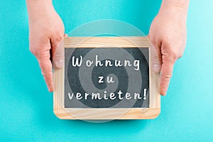 Holding a chalkboard in the hands, apartment for rent is standing in german language on the sign, moving to a new home