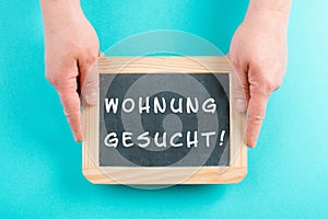 Holding a chalkboard in the hands, looking for an apartment is standing in german language on the sign, moving to a new home, real