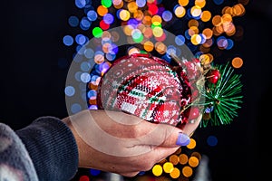 Holding Christmas bauble decoration isolated on background with blurred lights. December season, Christmas composition