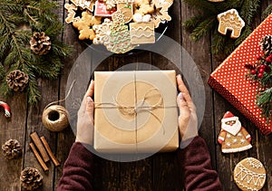 Holding a Christmas present on a wooden table decorated with winter holiday shaped cookies and various other ornaments, merry