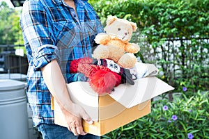 Holding clothing donation box with used clothes and doll at home to support help for poor people in the world