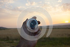 Holding a compass on the background of fields at sunset