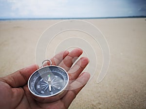 Holding a compass showing the direction point to north and facing the ocean.