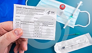 Holding a Covid-10 vaccination record card with vaccine vial, syringe and facial mask and faqs