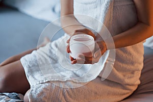 Holding creme. Time for a make up. Woman sits on the bed and use cosmetics to clean her skin