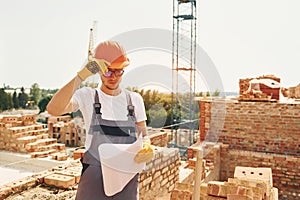 Holding document. Young construction worker in uniform is busy at the unfinished building