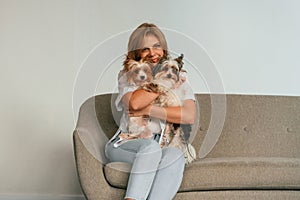 Holding and embracing the animals. Woman is sitting on a sofa with two cute dogs