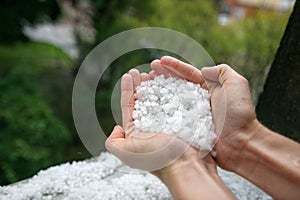 Holding freezing granulated hail ice crystals, grains in hands after strong hailstorm in autumn, fall.