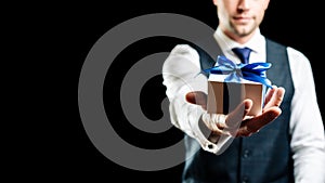 Holding gift box. Happy young business man holding surprise giftbox present with blue ribbon isolated on black