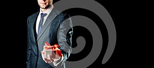 Holding gift box. Happy young business man holding surprise giftbox present with red ribbon isolated on black background