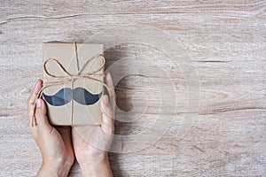 Holding gift box with mustache on wooden background, preparation for fathers. World International men day and Fatherâ€™s day