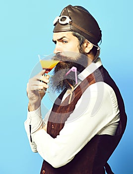 Holding glass of alcoholic beverage in vintage suede leather waistcoat with hat and glasses on red studio background