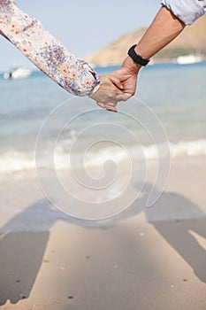 Holding hands couple on beach with shadow.