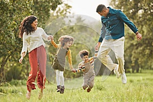 Holding hands, park and parents jump with children in nature for playing, bonding and fun together in field. Happy