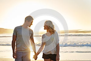 Holding hands, sunset and couple with love at beach, ocean and sea for affection, bonding or to relax. People, partners