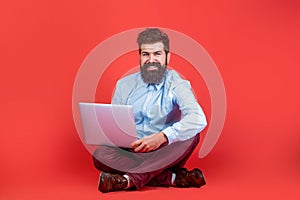 Holding laptop computer. Smiling handsome bearded man worker laptop. Happy young man sitting on the floor with and using
