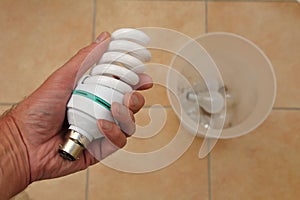 Holding a low energy CFL light bulb with discarded tungsten bulbs in background