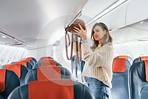 Holding lugagge. Young female passanger in casual clothes is in the plane photo