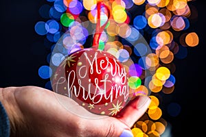Holding Merry Christmas bauble decoration isolated on background with blurred lights. December season, Christmas composition