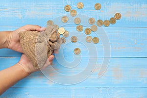 Holding money sack or bag with coins on blue wooden background