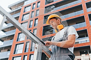 Holding notepad with plan. Young man working in uniform at construction at daytime