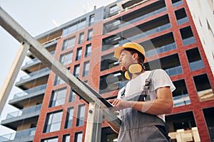 Holding notepad with plan. Young man working in uniform at construction at daytime